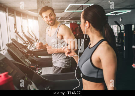 Fille mince et strong guy sont en cours d'exécution sur la machine de course. Ils parlent ensemble et profiter de l'instant. Close up. Banque D'Images