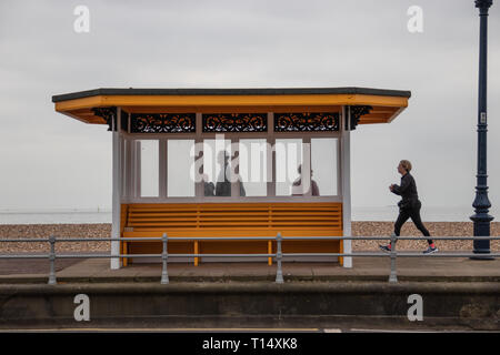 Les gens se tenait dans un abri de plage avec jogger passant par, Southsea, UK Banque D'Images