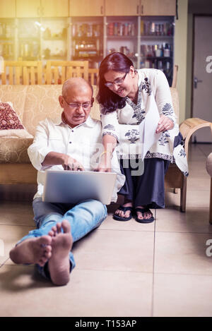 Un couple indien/asiatique senior qui effectue des opérations de financement à domicile et vérifie les factures avec un ordinateur portable, une calculatrice et de l'argent tout en étant assis sur un canapé à la maison Banque D'Images