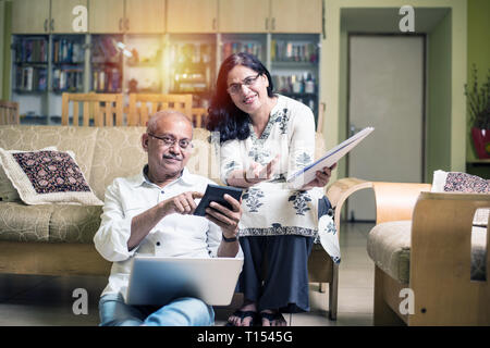 Un couple indien/asiatique senior qui effectue des opérations de financement à domicile et vérifie les factures avec un ordinateur portable, une calculatrice et de l'argent tout en étant assis sur un canapé à la maison Banque D'Images