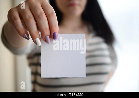 Jeune fille triste montre un autocollant blanc. Caucasian brunette tenant une feuille de papier vierge comme modèle pour votre texte