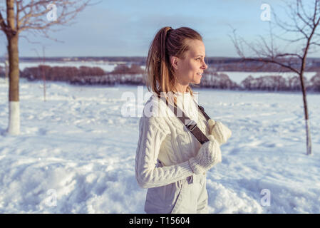 Une jeune fille de l'hiver dans la ville s'oppose à fond de la neige et des arbres. Espace libre pour le texte. En combinaisons blanches et mitaines chaudes. Banque D'Images