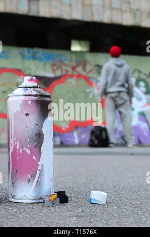 Peinture aérosol spray peut utilisé avec la peinture blanche et rose se trouvent sur l'asphalte à l'encontre de l'article guy devant un mur peint en dessins graffiti Banque D'Images