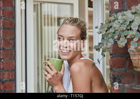 Portrait of smiling young woman sportive avec une tasse de café à l'entrée de la maison Banque D'Images