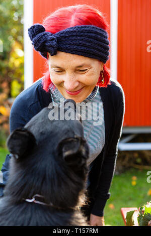 Portrait of smiling senior woman avec les cheveux teints en rouge face à face avec son chien dans le jardin Banque D'Images