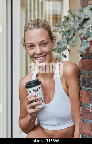 Portrait of smiling sporty woman avec boisson à emporter à l'entrée de la maison Banque D'Images
