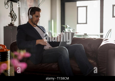 Écouteurs avec l'homme assis sur la table à l'aide d'ordinateur portable et téléphone cellulaire Banque D'Images