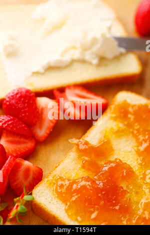 Répandre le fromage à la crème sur pain blanc avec de la confiture et des fraises aux côtés Banque D'Images