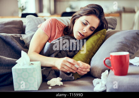 Portrait de jeune femme malade allongé sur couverts dans le contrat cadre d'essayer de prendre des pilules pour le froid Banque D'Images