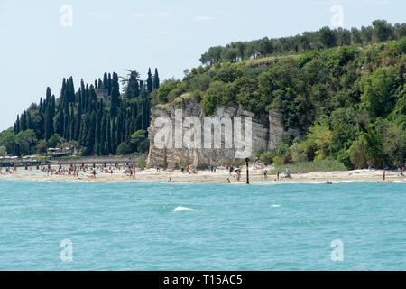 Plage de galets de la ville de Sirmione sur le lac de Garde avec vue sur les Grottes de Catulle (Grotte di Catullo), les ruines d'une villa romaine construite à la fin du 1 Banque D'Images