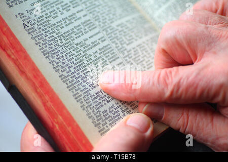 Un homme tient une Bible vintage et utilise ses doigts pour suivre les mots Banque D'Images