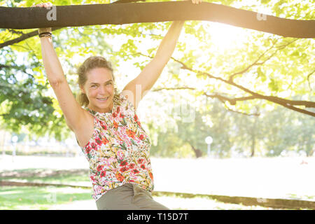 Portrait of smiling mature woman top avec floral design s'amusant dans un parc Banque D'Images