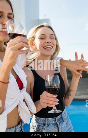 Copines sur une terrasse sur le toit, s'amuser à la piscine, boire du vin rouge Banque D'Images