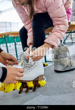 Mère d'aider sa fille à mettre sur des patins à glace Banque D'Images