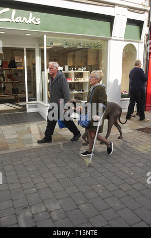 Femme handicapée passant devant un magasin de chaussures Clarks avec grand chien de Dane à Beverley Market, marché du samedi, East Yorkshire, Angleterre, Royaume-Uni, GB. Banque D'Images