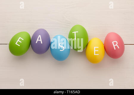 Les oeufs peints colorés avec des lettres disposées en un mot Easter sur planches en bois blanc arrière-plan. Maison de concept. Banque D'Images