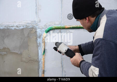 Un vieil ouvrier perce un trou dans un mur en polystyrène pour l'installation ultérieure d'une armature en plastique goujon. La création de trous dans le mur avec un Banque D'Images
