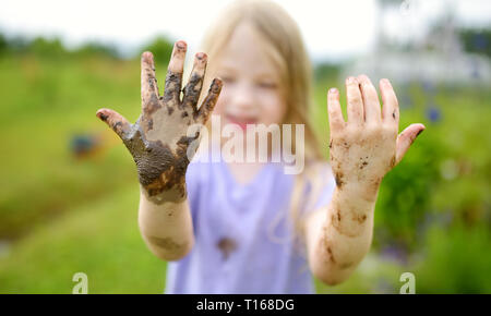 Funny little girl playing dans une grande flaque de boue humide par beau jour d'été. Enfant de se salir en creusant dans le sol boueux. Jeux en plein air. malpropre Banque D'Images