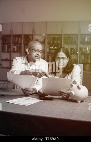 Un couple indien/asiatique senior qui effectue des opérations de financement à domicile et vérifie les factures avec un ordinateur portable, une calculatrice et de l'argent tout en étant assis sur un canapé à la maison Banque D'Images