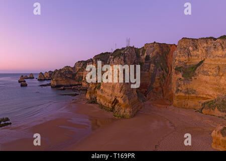 Plage de sable vide avec fantaisie cliffs au lever du soleil à Lagos, Portugal. Nuageux lever du soleil sur l'océan Atlantique. Banque D'Images