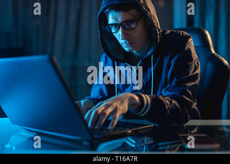 Mâle dans le capot à la recherche dans l'appareil photo. Les attaques de pirates et le vol d'accéder aux bases de données avec des mots de passe. Le concept de la cybersécurité Banque D'Images