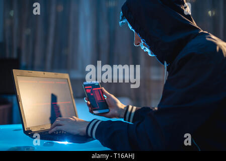 Homme hacker dans le capot de tenir le téléphone dans ses mains essayant de voler des bases de données Access avec des mots de passe. Le concept de sécurité cybernétique Banque D'Images