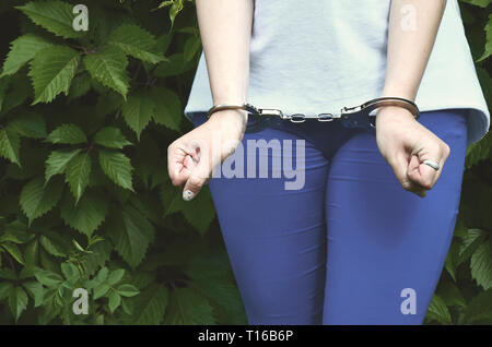 Fragment d'une jeune fille avec le corps criminel dans les mains des menottes contre un arrière-plan vert feuilles de lierre en fleur. Le concept de détention d'un offende Banque D'Images