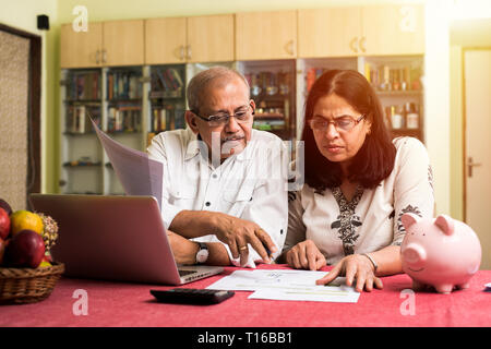 Un couple indien/asiatique senior qui effectue des opérations de financement à domicile et vérifie les factures avec un ordinateur portable, une calculatrice et de l'argent tout en étant assis sur un canapé à la maison Banque D'Images