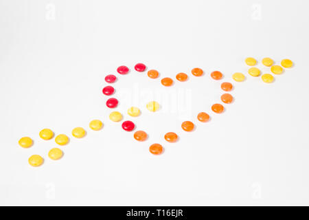 Forme de cœur percé d'une flèche comme symbole de l'amour - fabriqués à partir de bonbons sucrés colorés - haut-Vue de côté - Fond blanc Banque D'Images