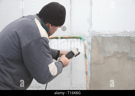 Un vieil ouvrier perce un trou dans un mur en polystyrène pour l'installation ultérieure d'une armature en plastique goujon. La création de trous dans le mur avec un Banque D'Images