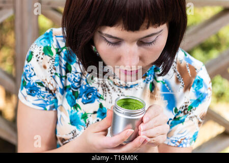 Thé vert matcha woman face closeup canister arôme odeur à l'extérieur dans jardin avec girl black hair Banque D'Images