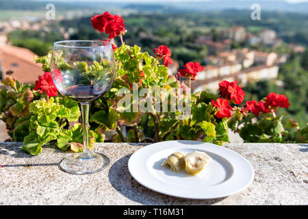 Gros plan du verre de vin rouge sur balcon terrasse par red geranium fleurs jardin extérieur en Italie avec vue sur la montagne dans la région de Chiusi, en Toscane et artichaut ap Banque D'Images