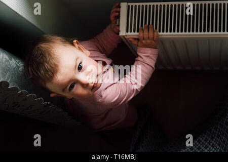 Portrait d'un adorable bébé près du radiateur à la maison Banque D'Images