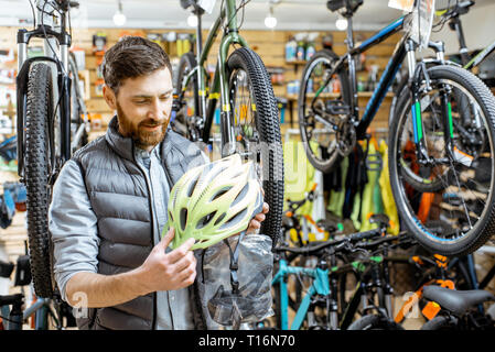 L'homme contrôle de la qualité d'un nouveau casque de protection debout dans le magasin de bicyclettes Banque D'Images