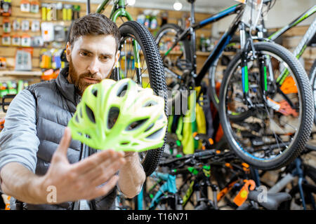 L'homme contrôle de la qualité d'un nouveau casque de protection debout dans le magasin de bicyclettes Banque D'Images