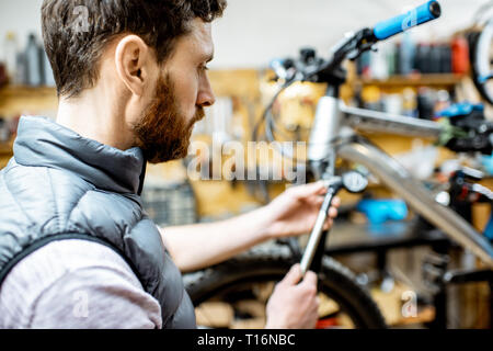 Réparateur au service d'une location, la vérification d'une pression de l'air dans l'amortisseur pneumatique d'une fourchette dans l'atelier Banque D'Images