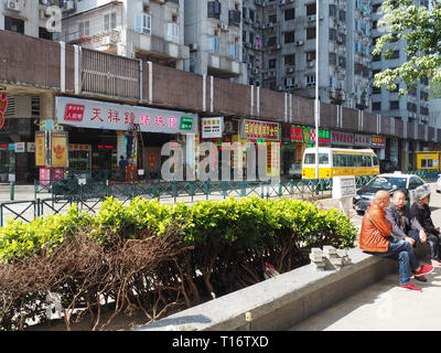 Macao, Chine - 2 novembre, 2017 : une rue tourné de trois personnes attendant l'autobus, avec plusieurs boutiques dans l'arrière-plan. Banque D'Images