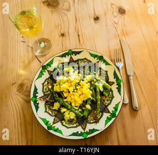 Un déjeuner léger d'Asperges Mimosa fait par des tranches d'œuf dur et d'échalotes servi sur une plaque fantaisie sur une table en bois Banque D'Images