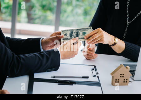 Vue latérale du petit gens d'affaires remise dollars avec maison décorative modèle de contrat at office Banque D'Images