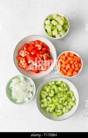 Les légumes frais, haché dans des bols en céramique sur un tableau blanc de cuisine pour la préparation de repas végétarien. Vue de dessus, copiez l'espace. Banque D'Images