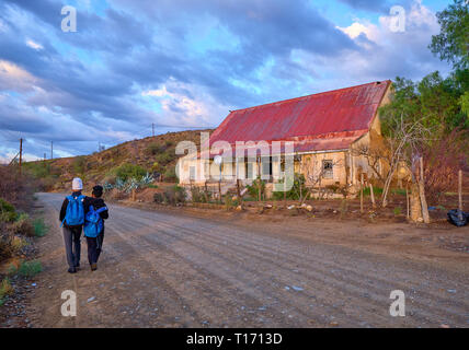 Karoo chemin de terre menant à un virage dans la lumière du matin. Deux adolescents vus de retour marchant à l'école, passant devant une ancienne maison de ferme à Calitzdorp Banque D'Images