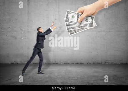 Vue latérale du businessman levant et maintenant les mains pour attraper cinq billets détenus par la main de l'énorme dans le coin supérieur droit. Banque D'Images