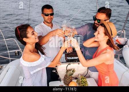 Deux couples se tenir en face de l'autre et à la vôtre avec des verres de champagne. Ils la regardent et sourire. Les gens de la voile sur le bateau. Banque D'Images