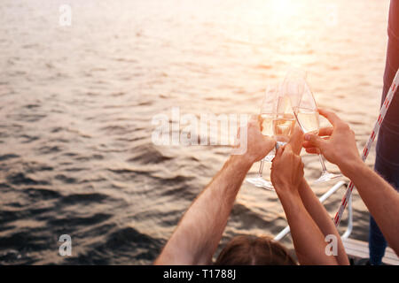 Belle photo de quatre mains tenant verres de champagne en face de l'eau. Ils ont un peu de repos. Il s'assombrit. Du soleil. Banque D'Images