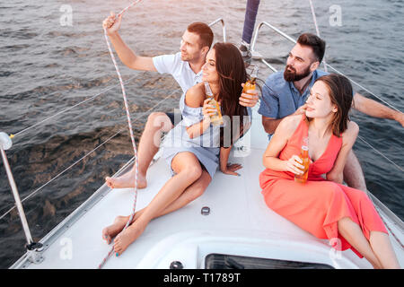 Deux couples sont assis sur la proue du bateau. Ils se tournent vers la gauche. Les femmes sont excired. Les hommes sont heureux aussi. Ils regardent sur le coucher du soleil. Banque D'Images