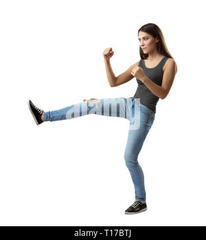 Vue latérale du jeune femme en débardeur et jeans avec des coups de pied de la jambe droite en avant et les bras en position de combat isolé sur fond blanc. Banque D'Images