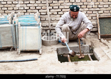 Vieux homme ouïghour écorce de mûrier de mélange soupe ' prêt à faire des feuilles de papier d'écorce de mûrier écrasée. La fabrication du papier de mûrier traditionnel, Hotan, Xinjiang Banque D'Images