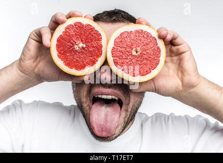 Drôle et bonne image de l'homme mettant deux adultes la moitié des morceaux de pamplemousse sur ses yeux. Il a également fait preuve de sa langue à la caméra. Isolé sur Banque D'Images