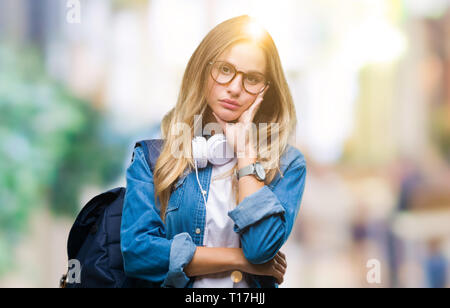 Belle jeune femme étudiante blonde portant des écouteurs et des lunettes plus de réflexion de fond isolé l'air fatigué et ennuyé par la dépression Les problèmes Banque D'Images