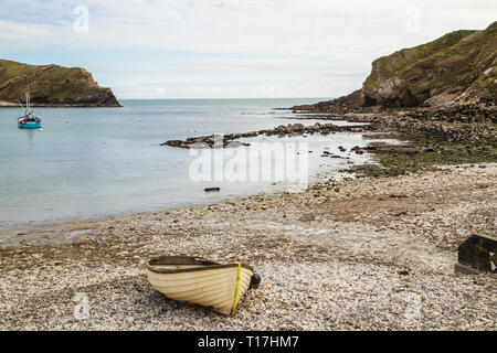 Un bateau à rames est situé sur la plage de l'anse de Lulworth et dans la mer il y a un bateau de pêche. Banque D'Images